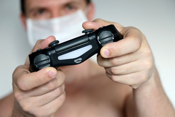 Man gamer in medical mask with gamepad playing video games. Joystick in male hands close-up, gaming addiction concept, home leisure at quarantine during covid-19 coronavirus pandemic