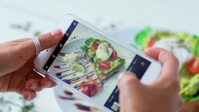 Female hands take photos of food on white table by modern smartphone. Closeup. 4K.