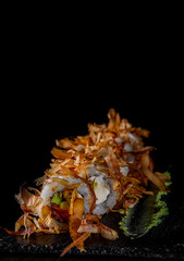 uramaki sushi rolls with cream cheese, fried salmon, tuna shavings, avocado  in plate on black wooden table background