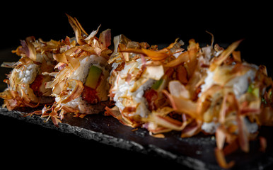 uramaki sushi rolls with cream cheese, fried salmon, tuna shavings, avocado  in plate on black wooden table background