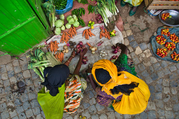 Black women in colorful traditional African costumes crouching at a vegetable stand on the ground...