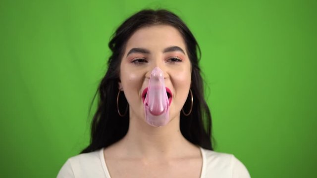 funny smiling girl chewing bubble gum, blowing pink bubble gum on green screen