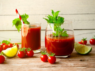 Tomato juice with fresh celery in glass, fresh cherry tomato and lime on a wooden table.