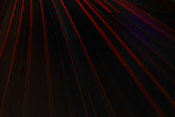 Rear red lights of a car in motion at long exposure on a night highway. Black background with red stripes.