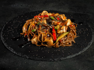 yaki soba. traditional asian buckwheat noodles with teriyaki chicken and fried vegetables. view from the top against a dark background. black slate dishes