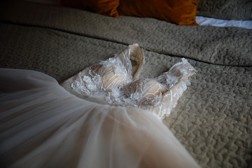 A beige wedding dress is lying on the bed in the room.