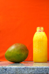 Glass bottles filled with colorful fresh homemade mango smoothies on an orange background