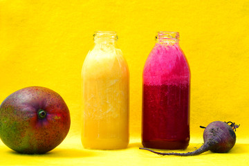 Glass bottles filled with colorful fresh homemade beet smoothies on a yellow background
