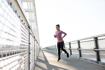 Beautiful fit woman in good shape jogging alone on city bridge.