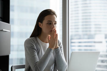 Superstitious millennial girl sit at desk in office hold hands in prayer ask beg about luck or good fate, religious young woman believer pray to god, believe in high power, faith, religion concept