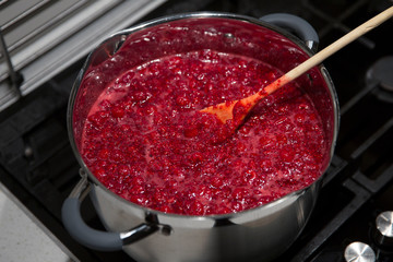 Cooking raspberry jam in a saucepan. Wooden spoon in a saucepan.