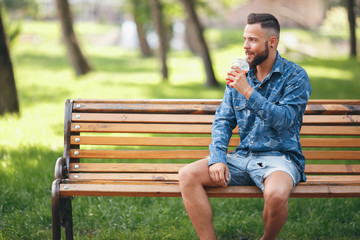 A guy with lemonade is resting in a park on a bench in the spring. Sunny day.