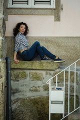 Multicultural woman sitting near the wall of the house in Porto, Portugal.