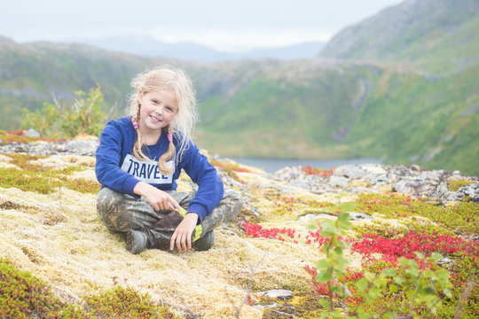 A girl sits in the mountains. In Norway. Beautiful, blonde, smiling. Summer day. Senya Island. Blurred background. Selective focus.