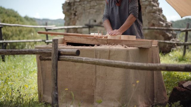 Close-up of medieval peasant making homemade fresh cheese inside round wooden cooking plate for trading on traditional village fair. Medieval artisan food on marketplace, lifestyle of middle ages