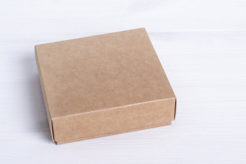 Blank cardboard box package isolated on white wood background. Craft paper box side view. Small square closed cardboard. Shipping eco package. Delivery pack. Gift idea, eco-lifestyle. Natural concept