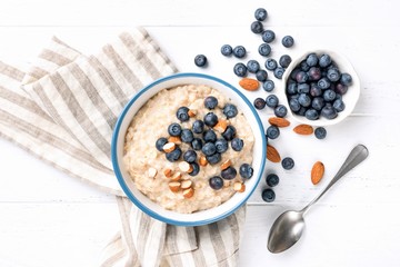 Oatmeal porridge with blueberries, almond nuts, table top view on white background. Healthy food,...