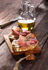 Bruschettas with cream cheese, prosciutto and rosemary on cutting board and wooden table
