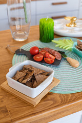 Close-up of slices of healthy crackers in white plate with fresh tomatoes cut on black board with sausage.