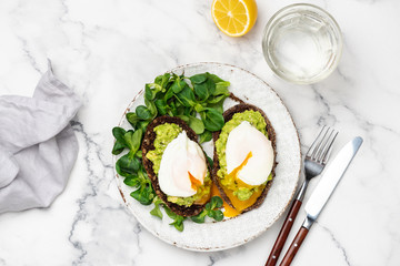 Tasty Healthy Breakfast Toast With Avocado And Poached Egg And Glass Of Pure Water On White Plate Over Marble Background. Table Top View