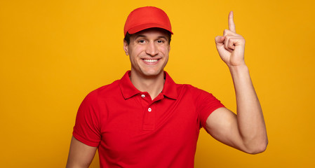 Naklejka premium Handsome young happy courier or delivery man in red uniform is posing isolated on yellow background.