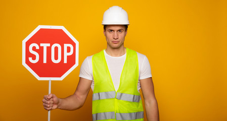 Close up photo of young serious and confident foreman or architect in build helmet with stop sign...