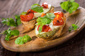 Bruschetta with tomatoes, mozzarella cheese, pesto and fresh basil on wooden background.