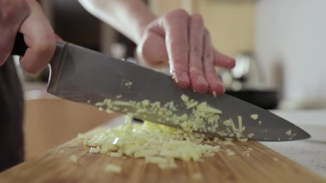 Woman chops garlic on a wooden cutting board, side view, close up