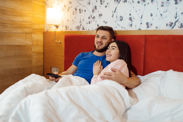Love couple lying in bed and watching TV