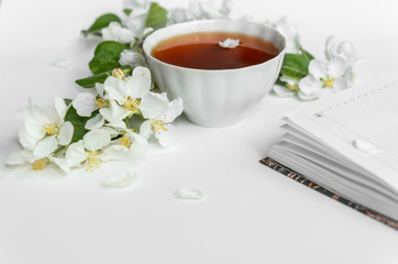Fototapeta na wymiar A cup of tea and a diary on the table. A branch of a blossoming apple tree. Flower petals