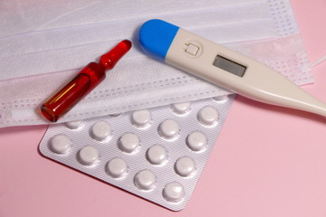 Аmpoule, tablets, thermometer and mask  against coronavirus on a pink background.