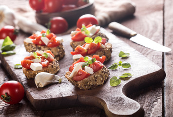 Bruschetta with tomatoes, mozzarella cheese and basil on wooden background.