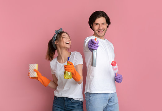 Joyful millennial couple posing with cleaning supplies on pink background