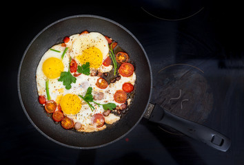 Homemade rustic fried eggs with tomatoes and bacon in a pan