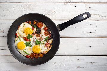 Homemade rustic fried eggs with tomatoes and bacon in a pan