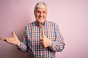 Naklejka premium Senior handsome hoary man wearing casual colorful shirt over isolated pink background Showing palm hand and doing ok gesture with thumbs up, smiling happy and cheerful
