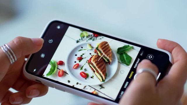 Female hands take photos of food on white table by modern smartphone. Closeup. 4K.