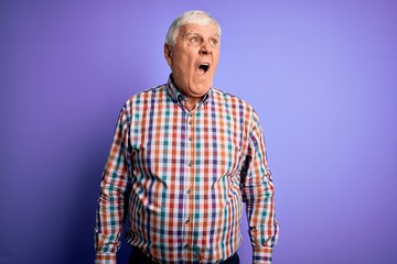 Senior handsome hoary man wearing casual colorful shirt over isolated purple background angry and mad screaming frustrated and furious, shouting with anger. Rage and aggressive concept.