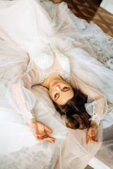 Cute bride in a pastel dress lies on the bed with her eyes closed
