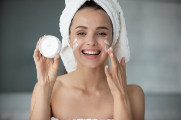 Smiling young woman in towel after shower use recommend moisturizing facial cream or mask, excited...