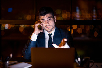 Displeased Entrepreneur Talking On Cellphone Sitting In Office At Night