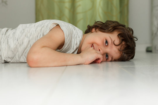 Curly boy lying on white floor at home and smiling. The concept of underfloor heating, quality laminate