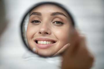 Close up of beautiful young woman look in mirror show healthy white teeth after dental treatment...