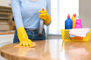 Young woman cleaning kitchen table using spray and rag