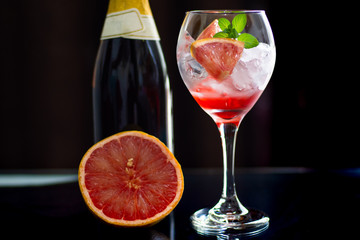 A fresh cocktail with a grapefruit and a bottle of wine on black background