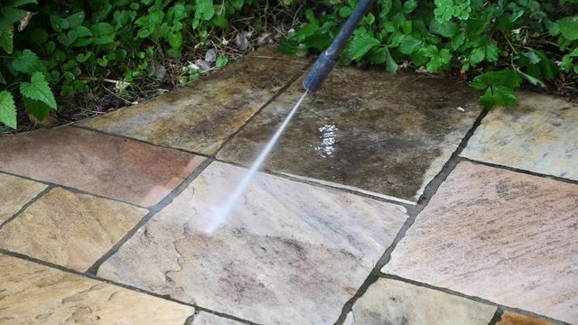 Mit einem Hochdruckreiniger die schmutzige Terrasse reinigen