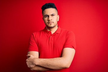 Young handsome man wearing red casual polo standing over isolated background skeptic and nervous, disapproving expression on face with crossed arms. Negative person.