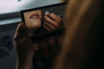 A young woman paints her lips while holding a mirror in her hands - 335907503