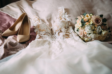Morning of the bride: the wedding dress, the bride's bouquet and shoes are lying on the bed - 335907559