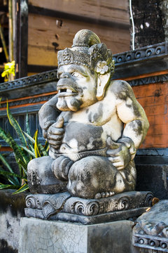 Traditional stone statue depicting demon sitting on front of temple. He has a terrible face. Art and culture at Bali, Indonesia